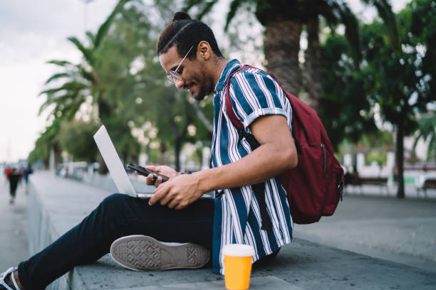 focused young ethnic male using laptop on street - hipster people surfing the net internet imagens e fotografias de stock