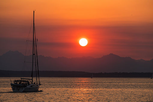 A spectacular orange sunset with swirling clouds and the silhouette of a sailboat sailing toward the sun in Potrero Costa Rica.