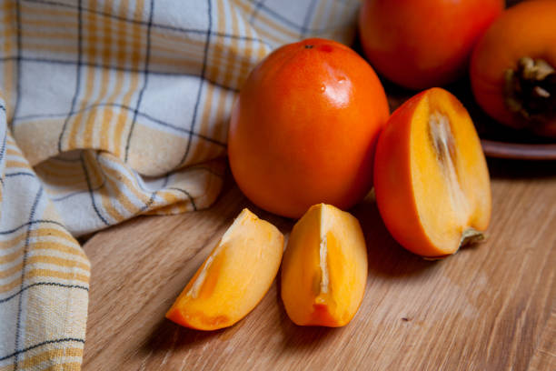 istock Whole ripe persimmon and sliced fruit on a wooden background. 1432435132