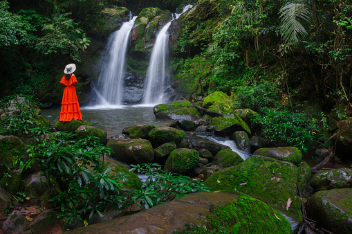 Beautiful woman in red dress in front of the Sapan Waterfall, Khun Nan National Park, Boklua District, Nan Province, Thailand.