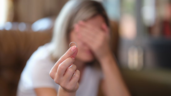 Woman holds wedding ring in hands and cries at home. Divorce depression and stress