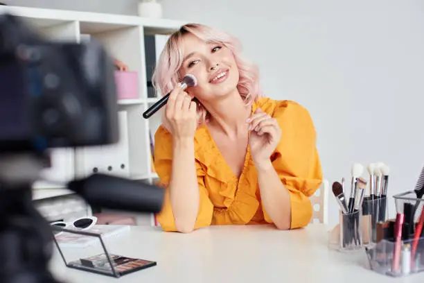 Photo of Pretty woman putting blusher on cheeks