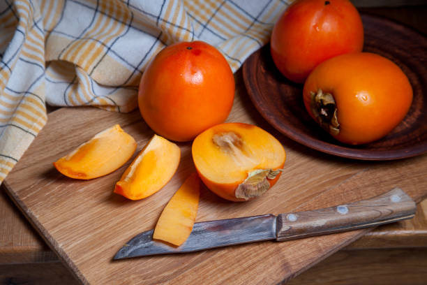 istock Whole ripe persimmon and sliced fruit on a wooden background. 1432442079