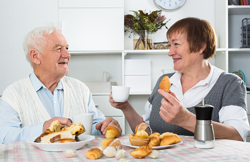Smiling elderly couple having breakfast and talking at table at home