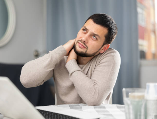 istock Man suffering from neck pain while sitting with laptop at home 1432443400