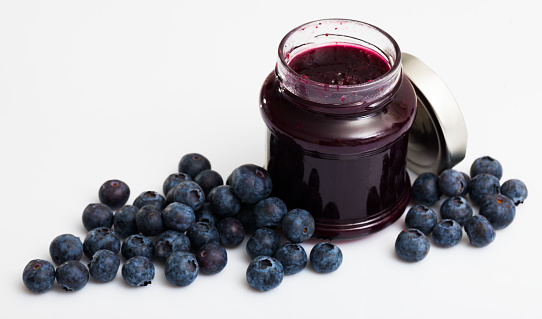 Homemade blueberry jam and fresh ripe blueberries on white background. Concept of healthy and diet food