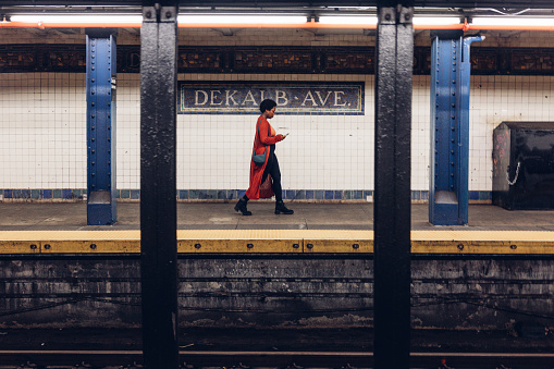 Woman in a subway station in Bushwick, Brooklyn - New York texting on mobile phone while waiting for her train to work