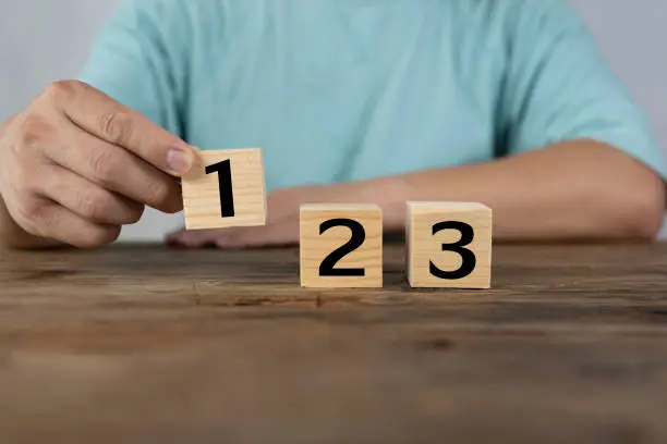 Close-up of a man holding a wooden block numbered one, two and three on a wooden table. concept wins