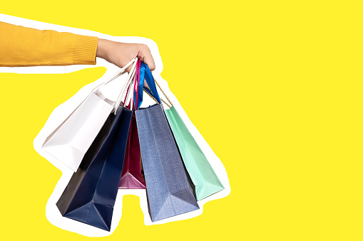 A hand holds paper bags for sale on a yellow background. Shopping concept. copy space
