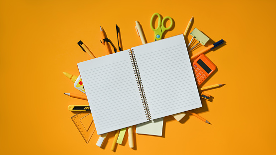Top view of notebook and various school supplies on yellow background, empty space ready for your design.