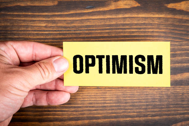 istock OPTIMISM. Piece of note paper with text in a man's hand. Wood texture background 1432464237