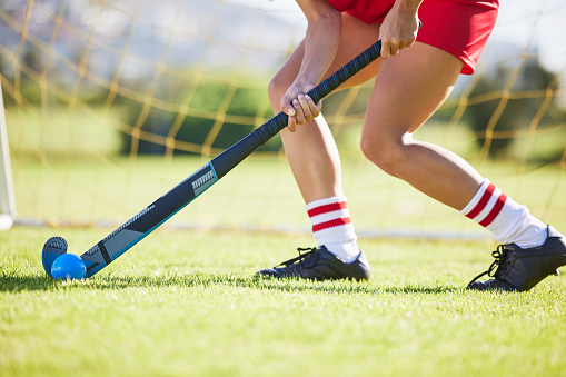 Looking down on a pair of wooden field hockey sticks wrapped one with red and the other with blue athletic tape with a white ball sitting on the turf.