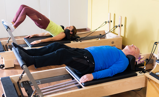 Older man doing exercises of remedial gymnastic on Pilates reformer in rehab clinic. Physical medicine concept