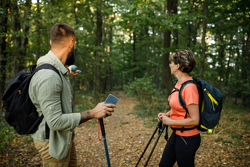 Side view of mature woman standing in the forest with her young son who is using a hiking pole and pointing at the trail route they should take.