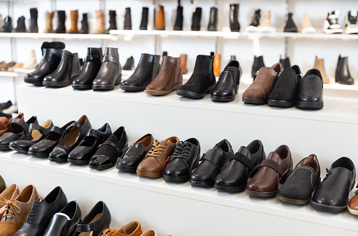 Diversity of leather and textile boots on shelves in salesroom of shoeshop.