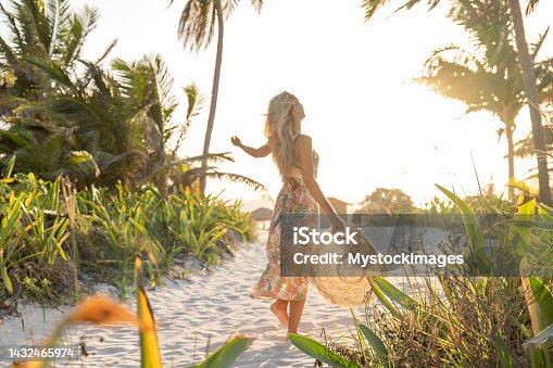 istock Young woman walks towards tropical beach at sunset, turns around herself for happiness 1432465974