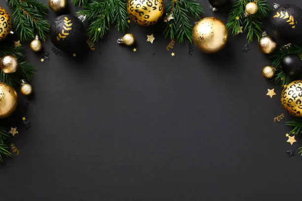 Photo of Merry Christmas greeting card template, frame, New Year banner design. Luxury gold baubles and fir branches on black background. Winter holidays composition. Flat lay, top view.