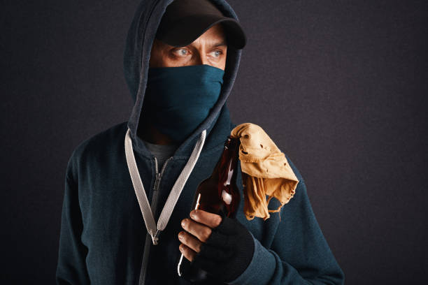 Male activist, rebel, riot wearing hoodie, cap and a face mask holding a bottle half full with flammable liquid known as Molotov Cocktail ready to throw. Violent street protest and chaos concept activista masculino, rebelde, antidisturbios con sudadera con capucha, gorra y una máscara facial que sostiene una botella medio llena con líquido inflamable conocido como cóctel molotov listo para lanzar. protesta callejera violenta y concepto de caos