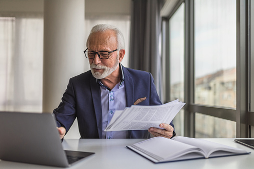 Bearded senior entrepreneur with eyeglasses, checking his work calendar on his laptop, at the boardroom.
