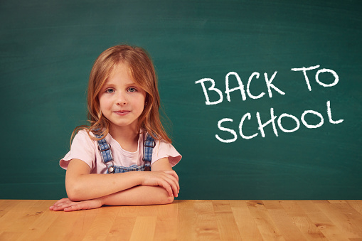 School child (girl) in classroom. Funny kid against green chalkboard. Idea and creativity concept. Copyspace on background. Back to school concept.