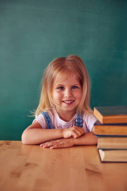 School child (girl) in classroom. Funny kid against green chalkboard. Idea and creativity concept. Copyspace on background. Back to school concept.