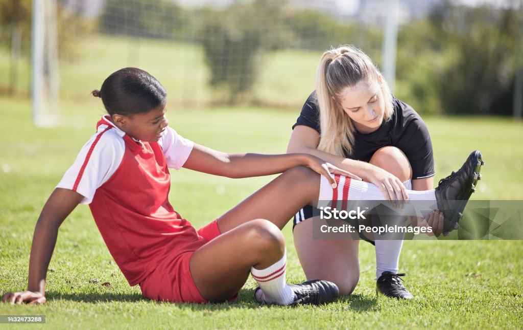 Soccer, sports and injury of a female player suffering with sore leg, foot or ankle on the field. Painful, hurt and discomfort woman getting her pain checked out by athletic trainer on the pitch. Athlete Stock Photo