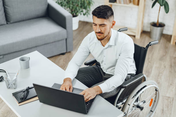 Positive disabled young man in wheelchair working in office stock photo