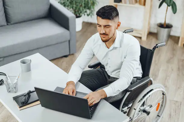 Photo of Positive disabled young man in wheelchair working in office