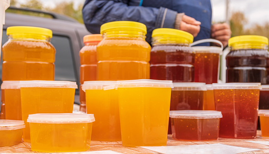 On counter is honey, packed in plastic containers of different sizes. Autumn agricultural fair.