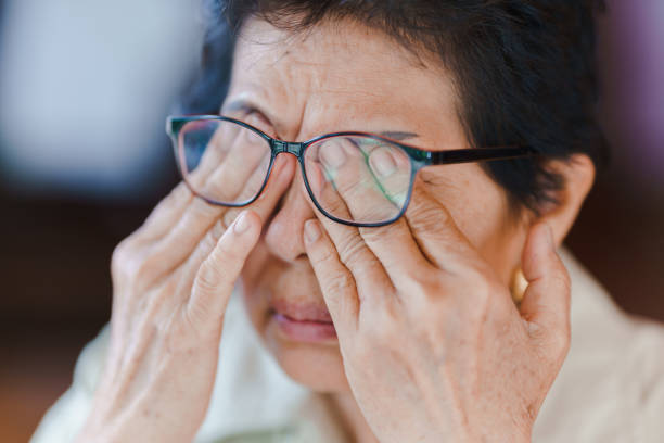una anciana usa anteojos y masajea sus ojos con las manos debido a la fatiga. concepto de problemas de salud en el anciano. - entrecerrar los ojos fotografías e imágenes de stock