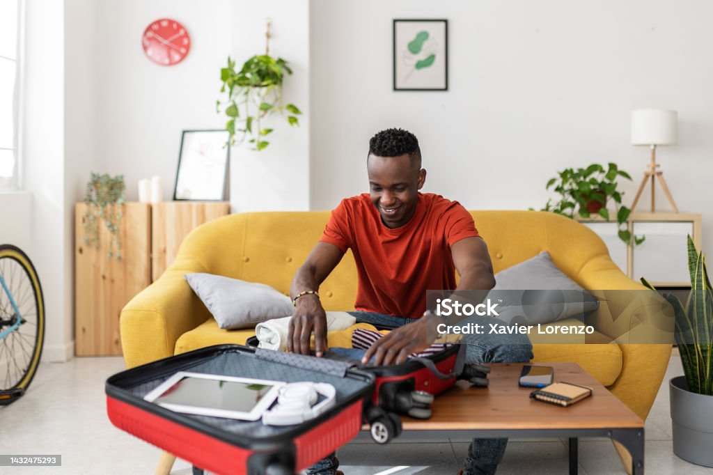 Young man packing travel bag for summer vacation Young man packing travel bag for summer vacation - African male preparing suitcase before going on holidays Suitcase Stock Photo