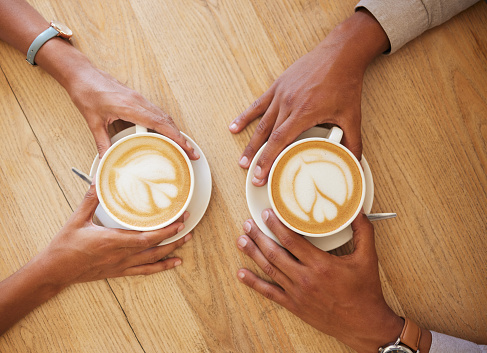 Creative latte art, cappuccino and coffee drink in cafe with couple and friends enjoying cup of java with milk froth together. Closeup of people hands from above meeting and drinking in restaurant