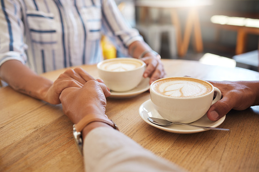 Coffee, break and dating couple holding hands on a romantic date at a cafe, restaurant or coffee shop. Man, woman or people touching, in love and romance on anniversary or valentines day together