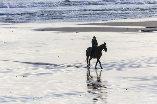 Distant wide shot of woman horseback riding along the beach in the North East of England. The scene is tranquil and calm.