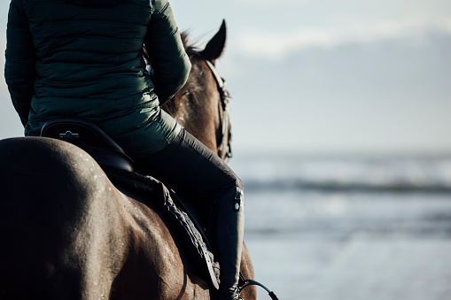 Rear view of an unrecognisable woman horseback riding along the beach in the North East of England. The scene is tranquil and calm. There is copy space available on the image.