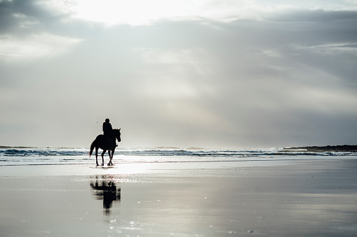 Woman horseback riding along the beach in the North East of England. The scene is tranquil and calm.