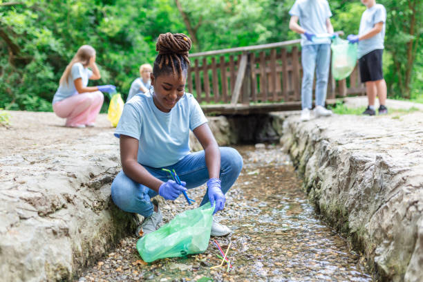 Woman handpicking gathering up garbage plastic straws garbage from the river at the park. World environment day.Environment concept.