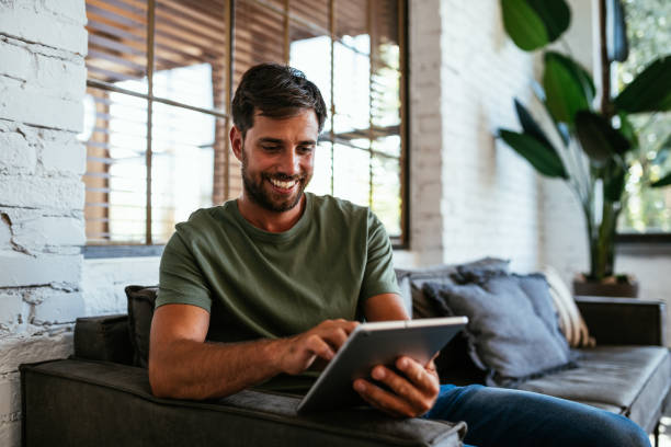 istock Millennial man sitting on couch and working on digital tablet 1432483328
