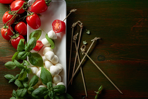 Mozzarella cheese with basil and tomatoes on a dark green wooden table. Top view.