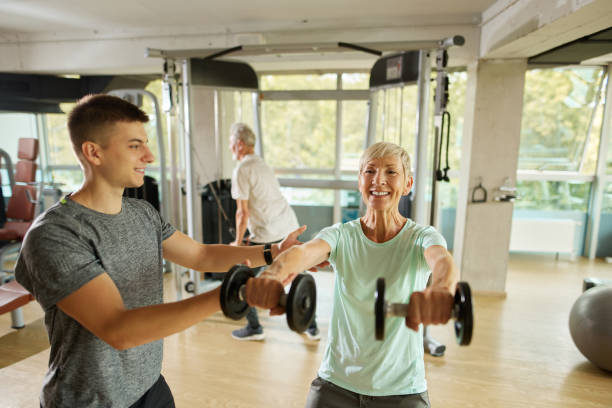 istock Senior woman exercising with personal trainer using dumbbells at the gym 1432492082