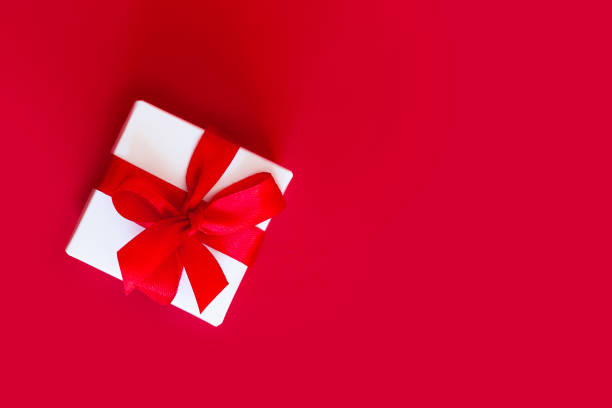 istock White box with a red ribbon on a red background, top view, copy space. Greeting card concept 1432492126