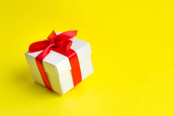 White box with a red ribbon on a yellow background, copy space. Greeting card concept. Gift concept