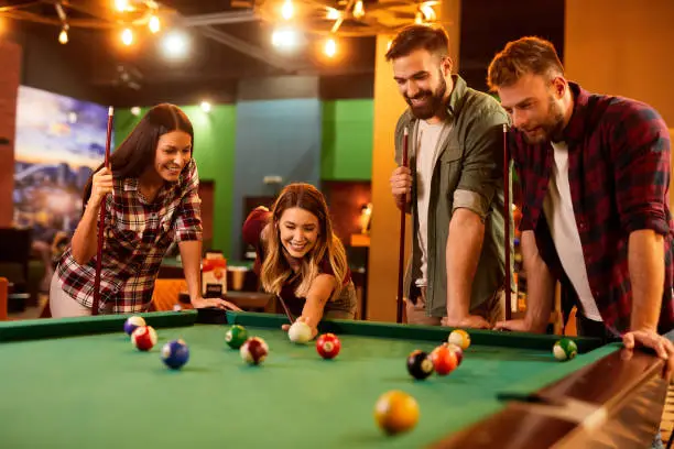 Group of friends having fun while playing pool in a local pool hall