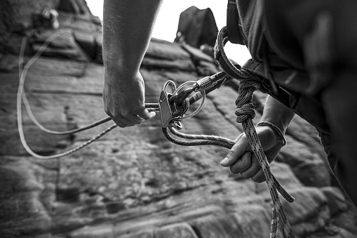 A grayscale shot of a person securing a harness around their waist to climb a mountain