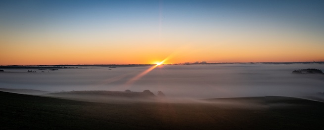 A panoramic view of a landscape covered with fog in Bjerget, Thy, Denmark at golden hour