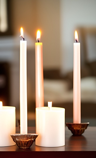 A vertical shot of three long burning candles on bronze candle holders on a table