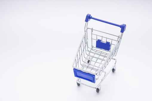 Mini shopping cart with a blue handle on white background. High angle of view. Space for text. Concept of shopping and e-commerce.