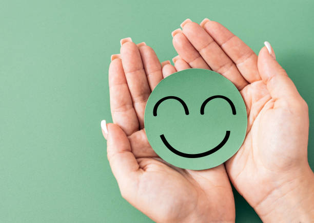 istock Hands holding a cardboard cutout smiley face on green background, satisfaction, well being, happiness, mental health, 1432499709