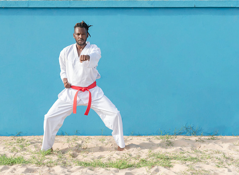 front view of a young African man training taekwondo outdoors on a blue background, martial arts concept