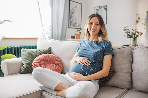Young expectant mother hugging  her baby bump and enjoying her morning in the Livingroom of her apartment;